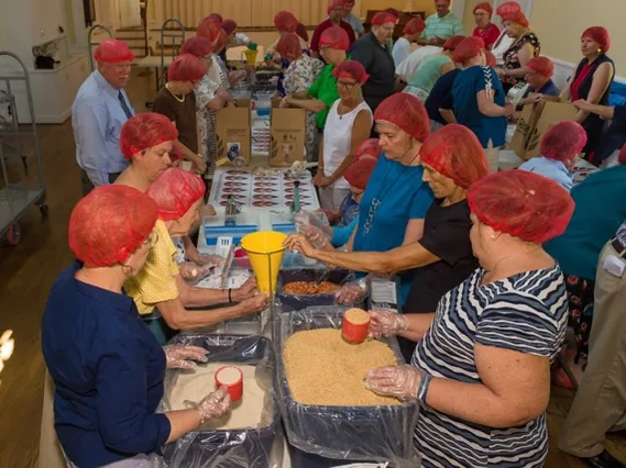 Volunteers in hairnets packing meals for hunger relief in the parish hall