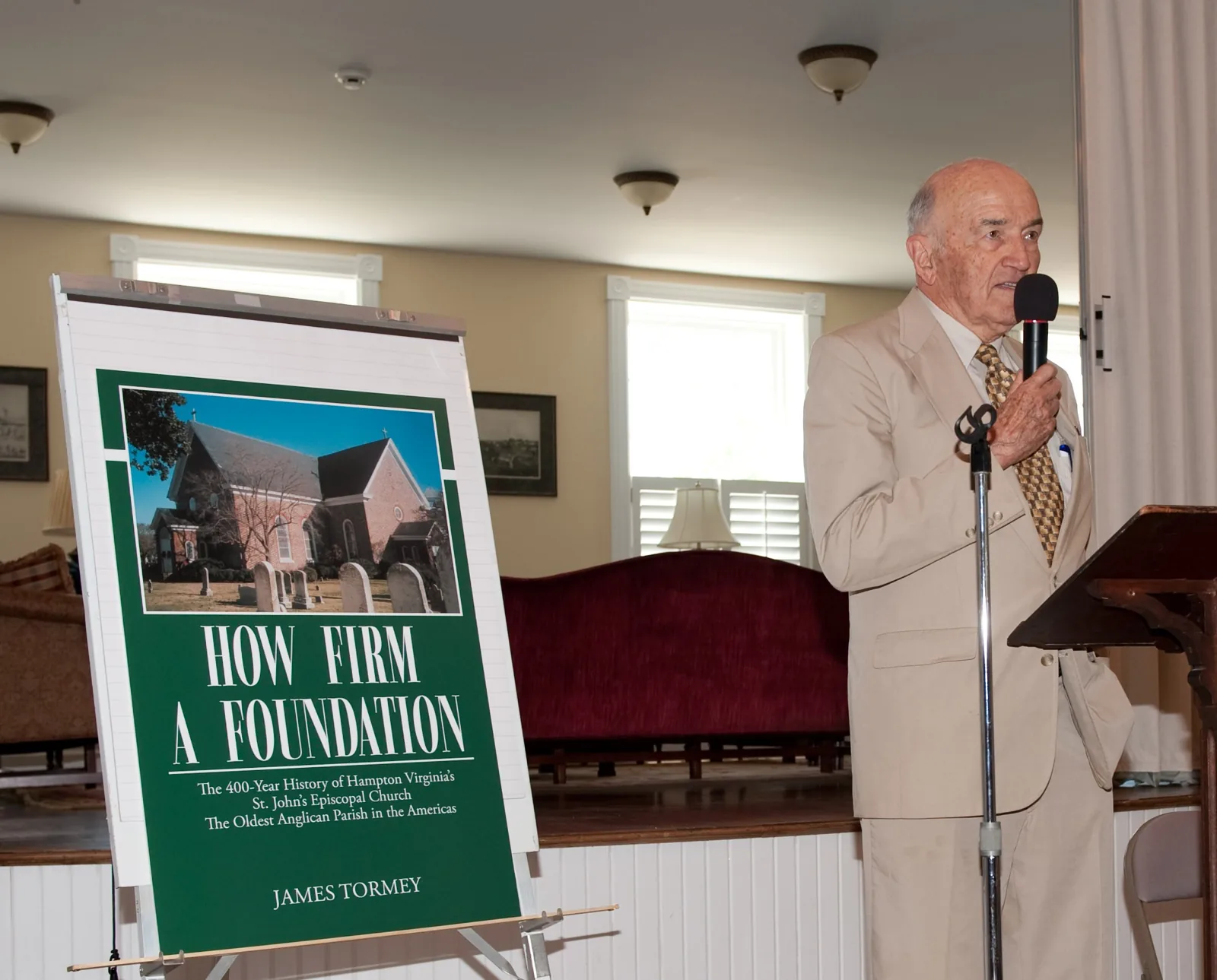 Jim Tormey speaking beside a poster of the cover of How Firm a Foundation