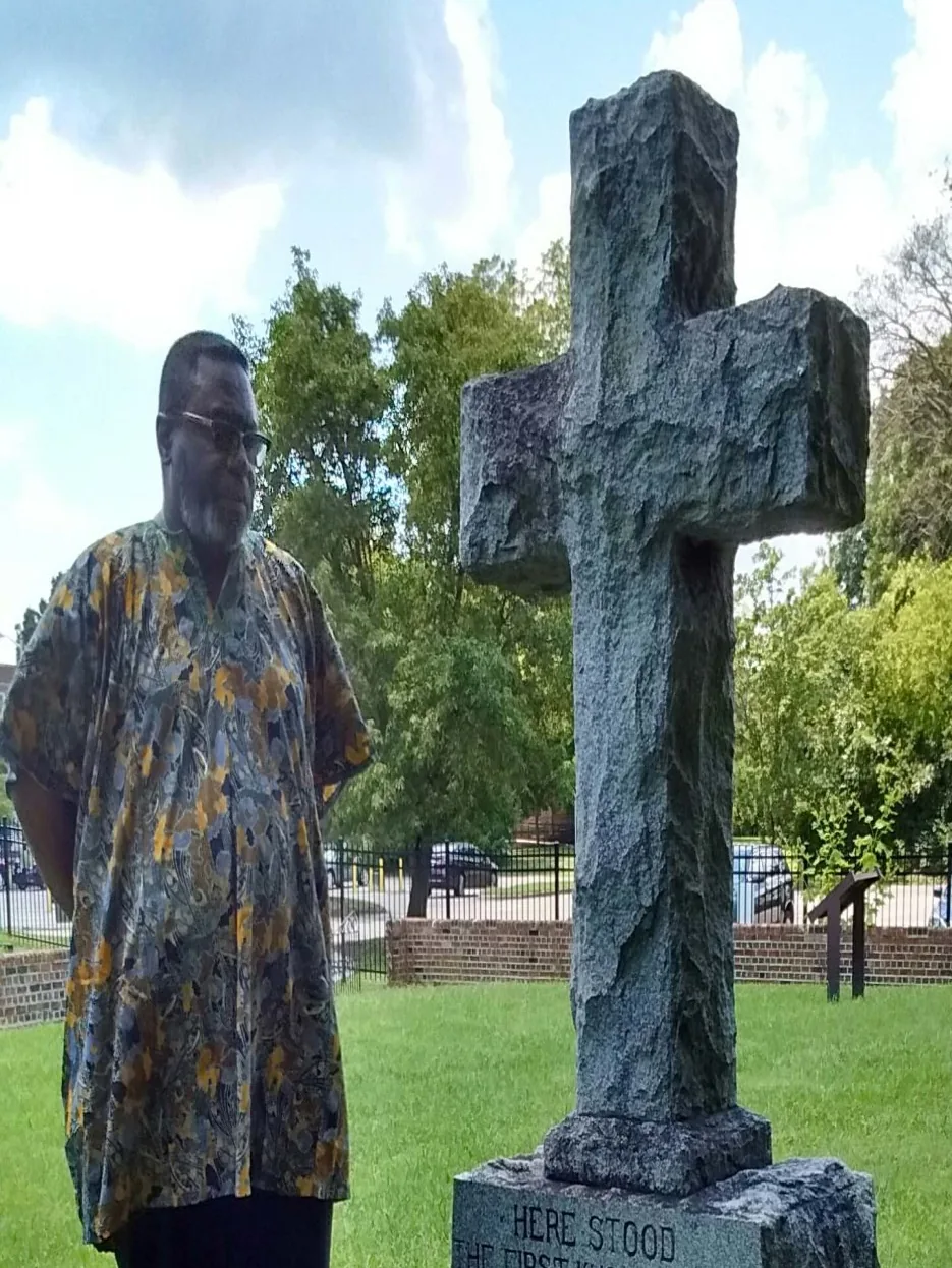 A visitor beside the cross at St. John's second church site
